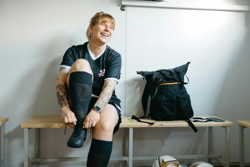 A female soccer player smiling while tying her shoelaces in a locker room.